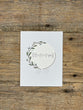 White card with decorative wreath and text on a wooden surface