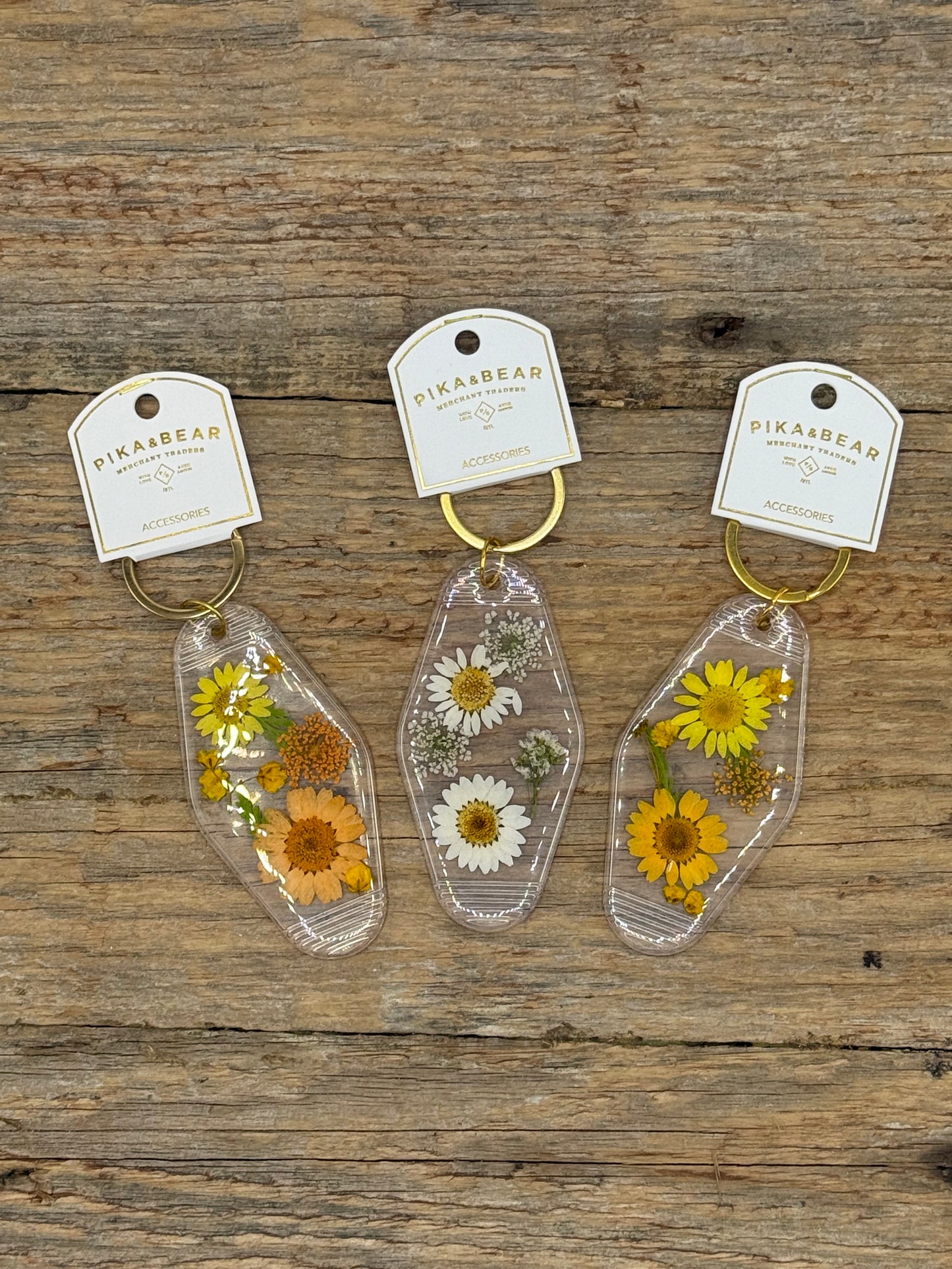 Three floral keychains on tags with 'Pika&Bear' branding on a wooden surface.