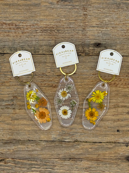 Three floral keychains on tags with 'Pika&Bear' branding on a wooden surface.