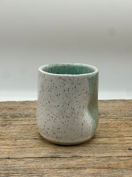 Speckled ceramic cup on a wooden surface with a white background