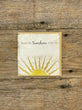 Card with sun design and text on a wooden surface