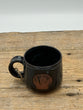 Black mug with a shell design on a wooden surface