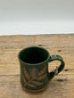 Green mug with leaf design on a wooden surface