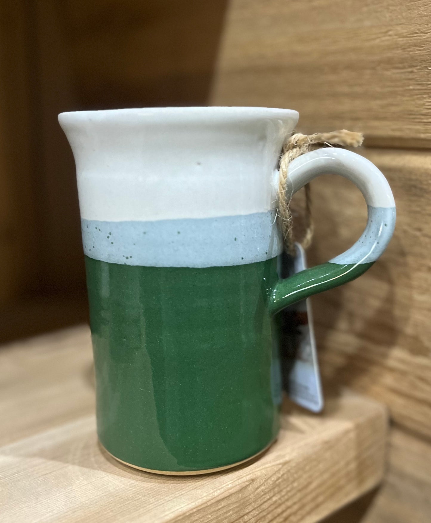 A ceramic pottery mug with a two-tone design, featuring a solid beige color at the bottom and a speckled white at the top, with a handle.