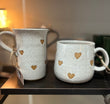 Two ceramic mugs with heart patterns on a wooden surface.